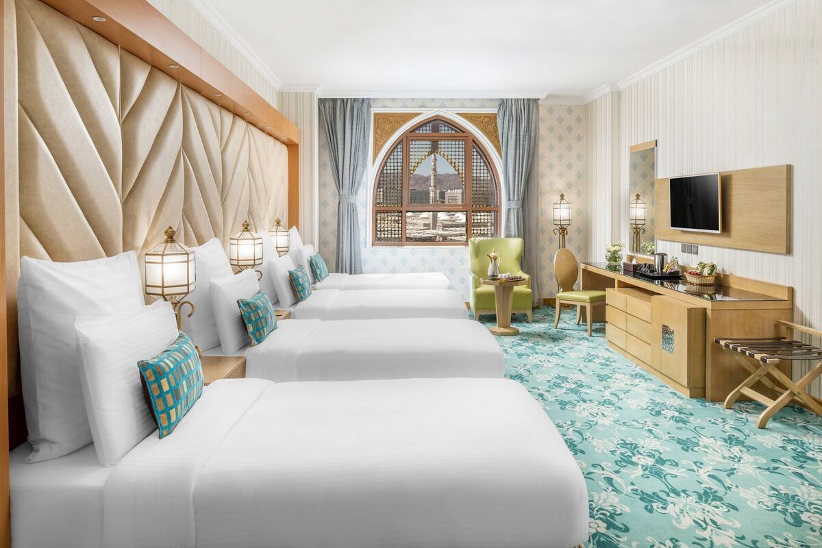 Une chambre d’hôtel avec trois lits, un bureau, une chaise et une télévision.