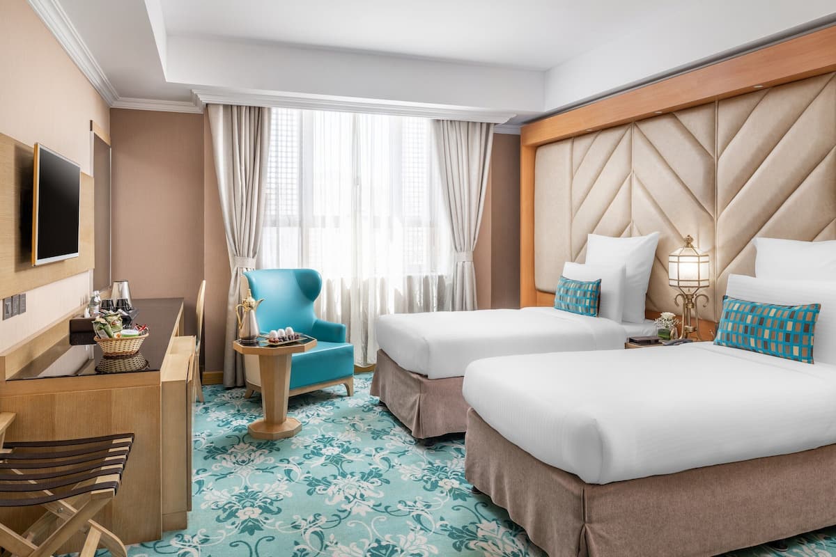 Une chambre d’hôtel avec deux lits, un bureau, une chaise, une télévision et une fenêtre avec des rideaux.