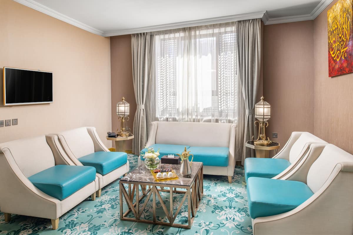 Une chambre d’hôtel équipée d’un canapé, d’une table basse, d’un téléviseur à écran plat et d’une fenêtre avec des rideaux légers.