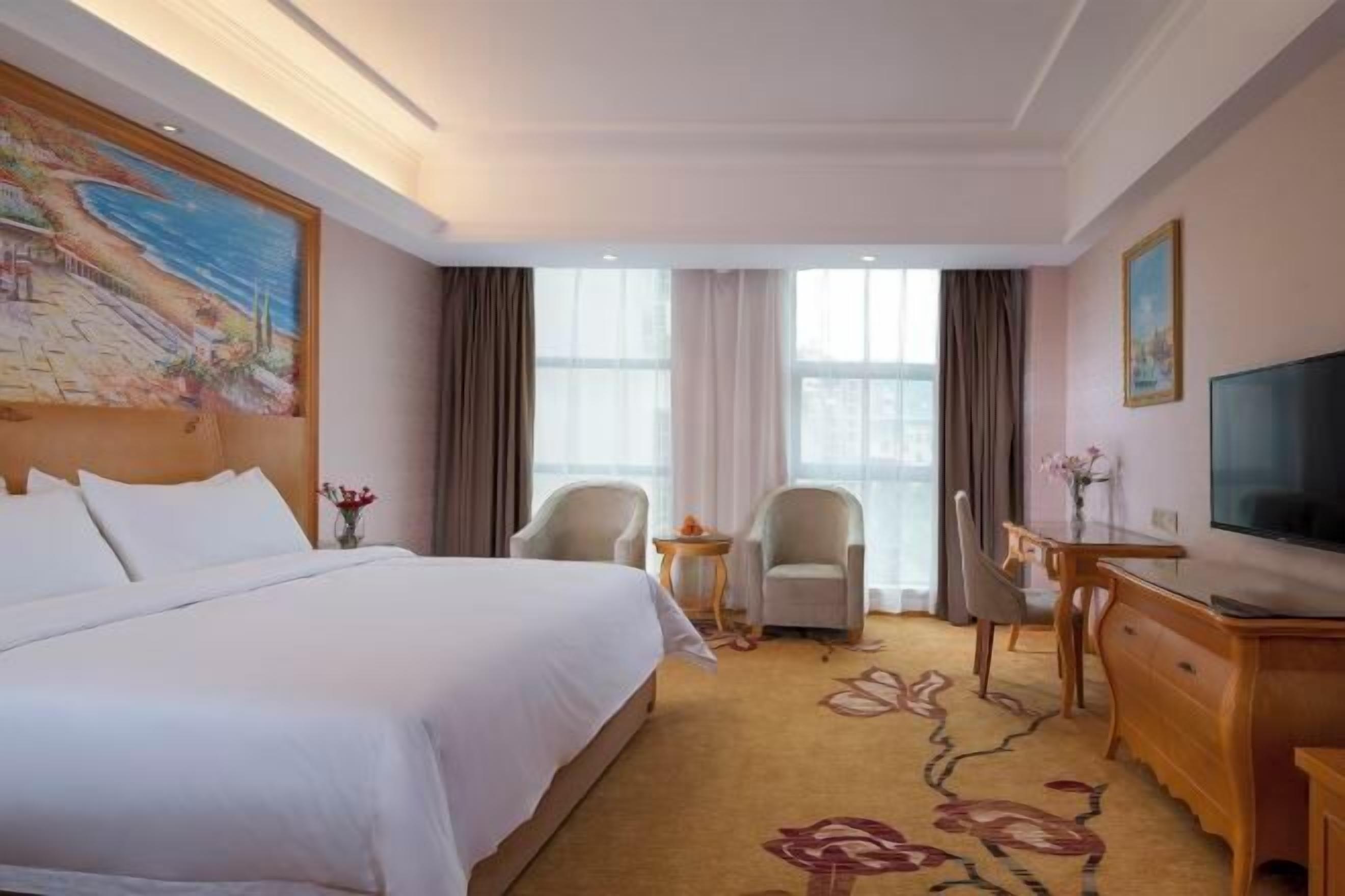 Una camera d'hotel con un letto grande, due poltrone, una scrivania, una televisione e un quadro appeso al muro.