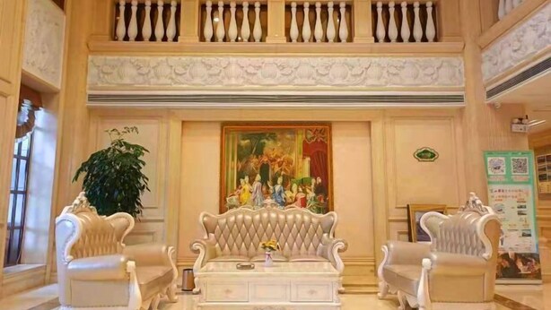 Eine beeindruckende Eingangshalle mit hoher Decke, aufwendigen Balustraden, einer zentralen Sitzecke mit gepolstertem Sofa und einem großen Gemälde darüber.