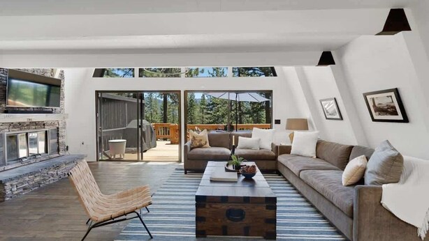 A modern living room with a stone fireplace, a sofa, a coffee table, and a view of the outdoors. - Incline Village Retreat: Hot Tub & Beach Access (Incline Village)