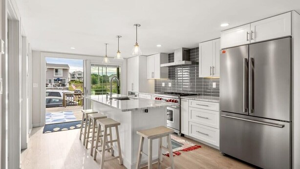 A modern kitchen with a central island, stainless steel appliances, and a view to the outside. - The Nest | High-End Kitchen | Steps to Beach | A/C (Newbury)