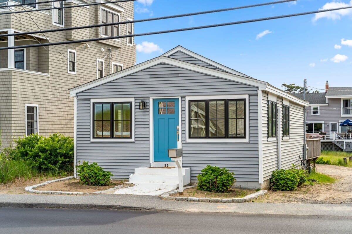 Une petite maison à un étage, avec une porte d’entrée bleue, des boiseries blanches et un petit porche.