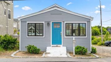 A small, single-story house with a blue front door, white trim, and a number '25' on the front steps.
