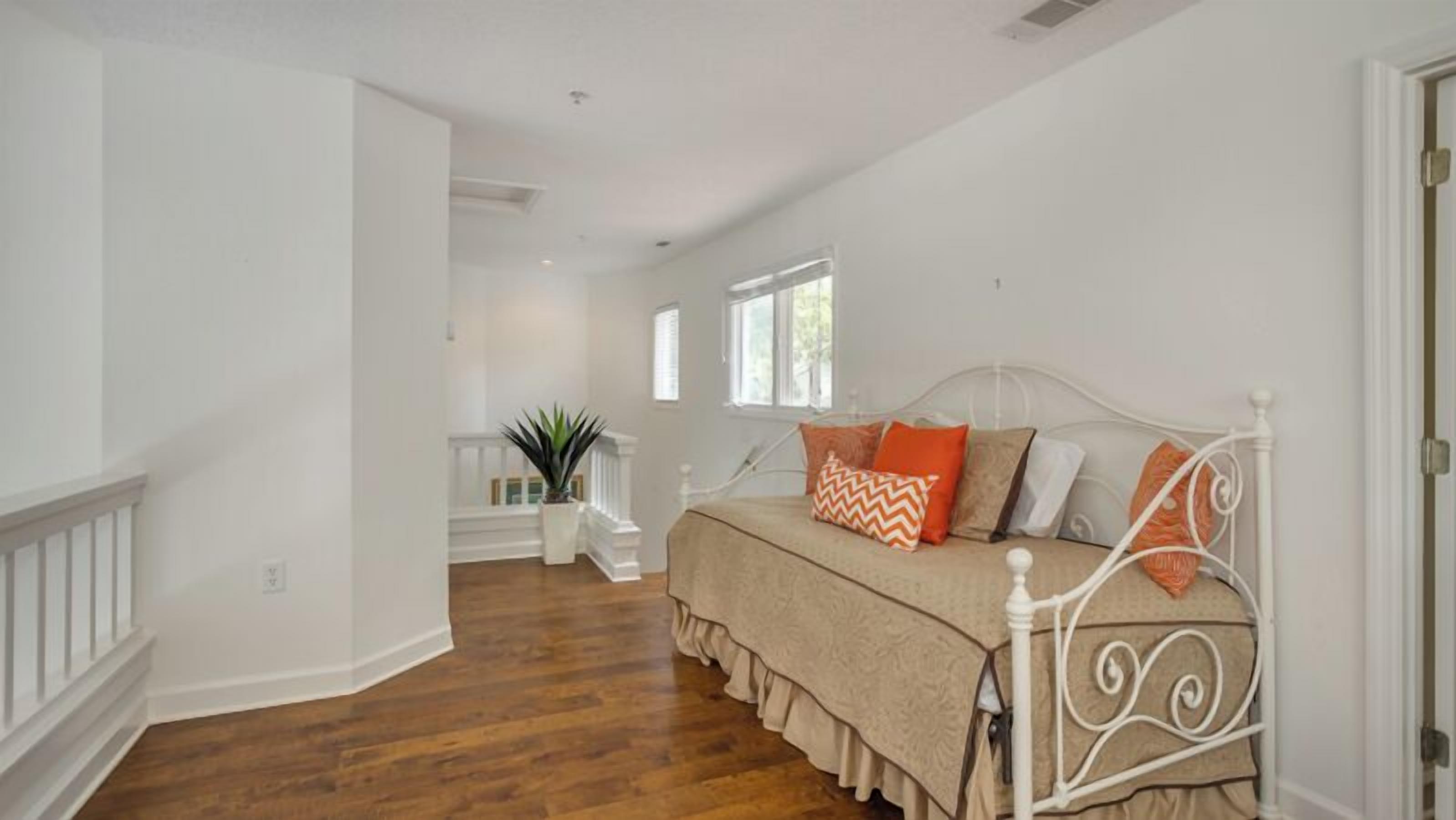 A bedroom with a white bed, a wooden floor, a white railing, and a window.
