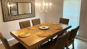 Een eetkamer met een grote houten tafel, zes stoelen, een kroonluchter en een decoratieve spiegel.