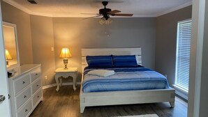 Een slaapkamer met een bed, nachtkastjes, een dressoir, een plafondventilator en een raam met jaloezieën.