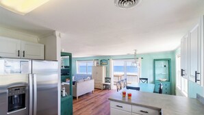 A compact kitchen with a stainless steel refrigerator, a water dispenser, and a dining area with a table and chairs. - Sweeping Ocean Views, Spectacular Sunrises, One-level living, KD3311 (Kill Devil Hills)