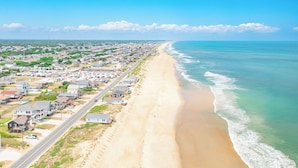 An aerial view of a coastal town with a long beach, houses, and a road running parallel to the shore. - Sweeping Ocean Views, Spectacular Sunrises, One-level living, KD3311 (Kill Devil Hills)