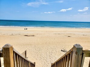 A beach with a wooden walkway leading to the water, sandy beach, and a clear sky.