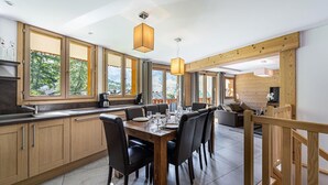 A modern kitchen with wooden cabinets, a dining table set for six, and large windows offering a view of the outdoors. - Wifi, ski-in/ski-out & foot of the slopes, Ground floor, balcony, parking, tv, 100m² (Saint-Martin-de-Belleville)