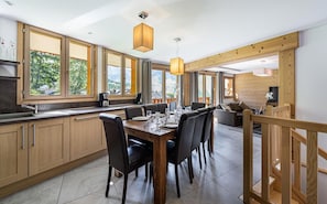 A modern kitchen with wooden cabinets, a dining table set for six, and large windows offering a view of the outdoors. - Wifi, at the foot of shops, Ground floor, balcony, parking, tv, 100m², Saint Martin de Belleville (Saint-Martin-de-Belleville)