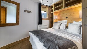 A bedroom with a bed, a large mirror, a window with curtains, and wooden shelving. - Wifi, ski-in/ski-out & foot of the slopes, Ground floor, balcony, parking, tv, 100m² (Saint-Martin-de-Belleville)