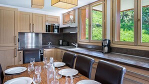 A modern kitchen with wooden cabinets, stainless steel appliances, and a dining area with a table set for four. - Wifi, ski-in/ski-out & foot of the slopes, Ground floor, balcony, parking, tv, 100m² (Saint-Martin-de-Belleville)