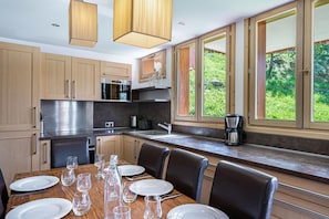 A modern kitchen with wooden cabinets, stainless steel appliances, and a dining area with a table set for four. - Wifi, at the foot of shops, Ground floor, balcony, parking, tv, 100m², Saint Martin de Belleville (Saint-Martin-de-Belleville)