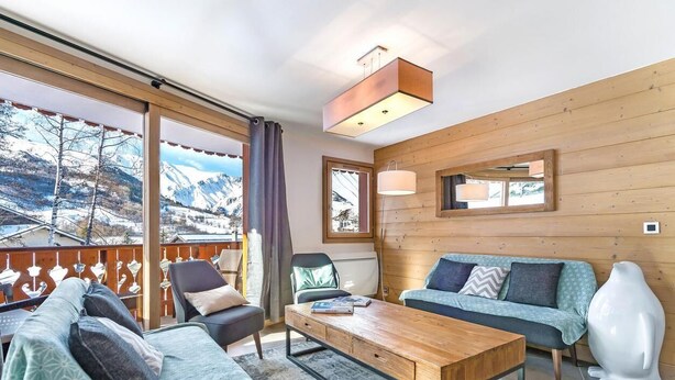 Ein gemütliches Wohnzimmer mit Holzboden, einer Couch, einem Couchtisch und einem großen Fenster mit Blick auf die Berge.