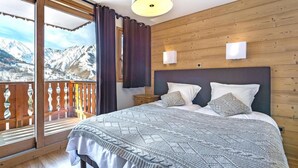 Ein Schlafzimmer mit einem großen Bett, Holzwänden, einem Balkon mit Blick auf schneebedeckte Berge und einer Deckenleuchte.