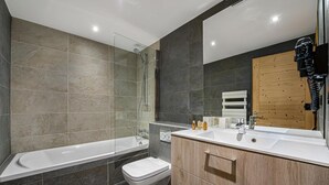 Une salle de bain moderne avec une douche à parois de verre, une baignoire blanche et un meuble-lavabo en bois doté d’un miroir.