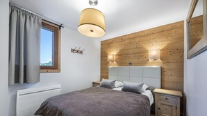 Une chambre à coucher comprenant un lit, des tables de chevet, une fenêtre avec des rideaux, un panneau mural en bois et un luminaire au plafond.
