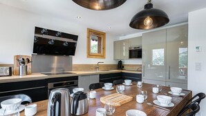 Une cuisine moderne dotée d’appareils électroménagers en acier inoxydable, une table à manger en bois agrémentée de vaisselle blanche et une grande fenêtre au-dessus de l’évier.