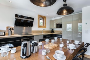 A modern kitchen with stainless steel appliances, a wooden dining table set with white dishes, and a large window above the sink.