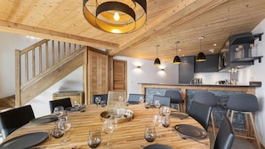 Un comedor con una mesa de madera dispuesta para seis personas, rodeada de sillas, y una escalera que sube a un nivel superior.