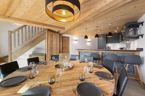 A dining area with a wooden table set for six, surrounded by chairs, and a staircase leading to an upper level. - Wifi, at the foot of shops, 3rd floor, balcony, fireplace or stove, parking, tv, 148m² (Saint-Martin-de-Belleville)