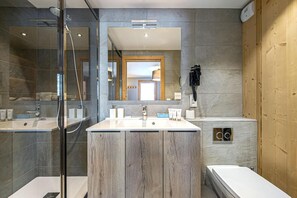 Un baño moderno con un espejo grande, dos lavamanos, ducha y pared de paneles de madera.