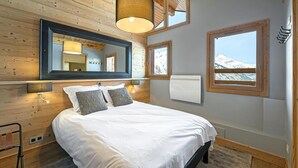 Un dormitorio con una cama grande, un espejo, una ventana con vistas a la montaña y paneles de madera.