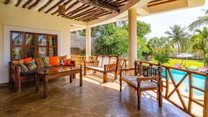 A covered outdoor seating area with wooden furniture and a view of a swimming pool. - Luxury Holiday Villa - Private Chef - Pool - A/C (partly) (Ukunda)