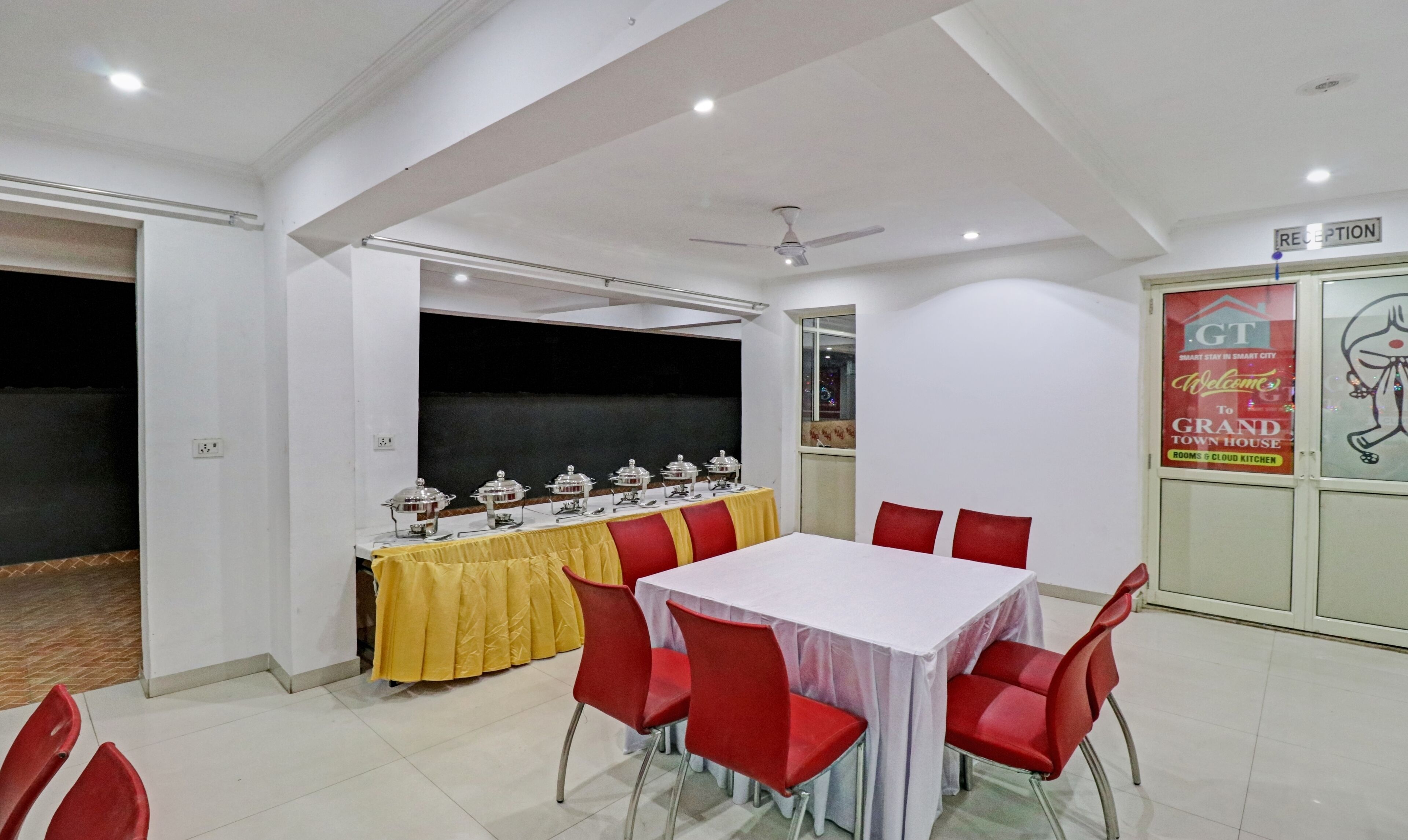 A conference room with a white table, red chairs, and a buffet table with covered dishes.