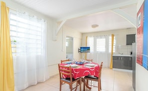 A dining area with a table set for four, a television mounted on the wall, and a kitchen area visible in the background.