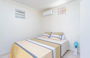 A bedroom with a bed, two pillows, a bedside lamp, and an air conditioning unit.