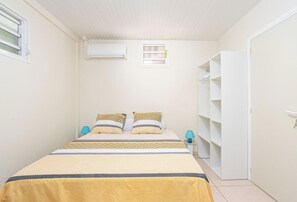A bedroom with a bed, two bedside lamps, a wardrobe, and an air conditioning unit. - Vauclin Émeraude - Appartement climatisé (Le Vauclin)