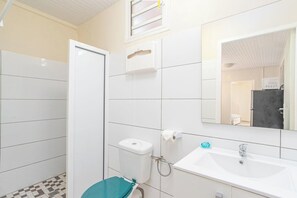 A bathroom with white tiles, a sink, a toilet, and a shower.