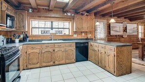 Une cuisine rustique avec des meubles en bois, un îlot central et une fenêtre ornée d’une inscription indiquant « MAISON AU BORD DU LAC ».