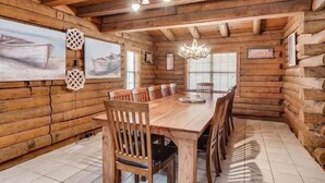 L'intérieur d'une cabane en rondins, avec une grande table à manger, des chaises en bois, un lustre et un tableau accroché au mur.