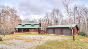 Une cabane rustique en rondins de bois, avec un toit végétalisé, une véranda et un garage.