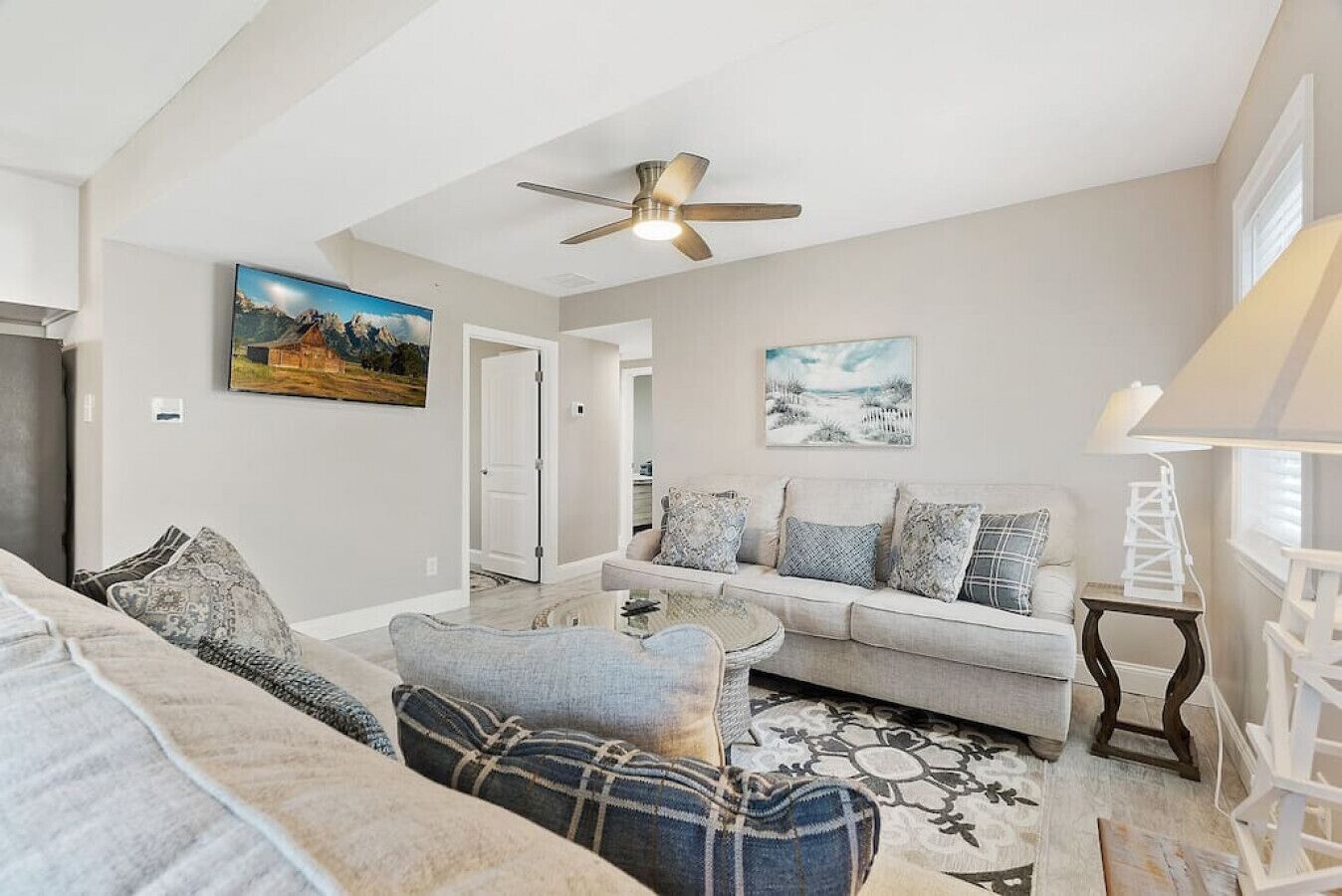 A living room with a sofa, a coffee table, and a ceiling fan. There are two paintings on the wall.