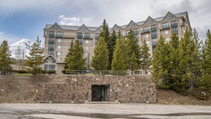 Un hotel de varios pisos con fachada de piedra, balcones y vistas a una montaña nevada.