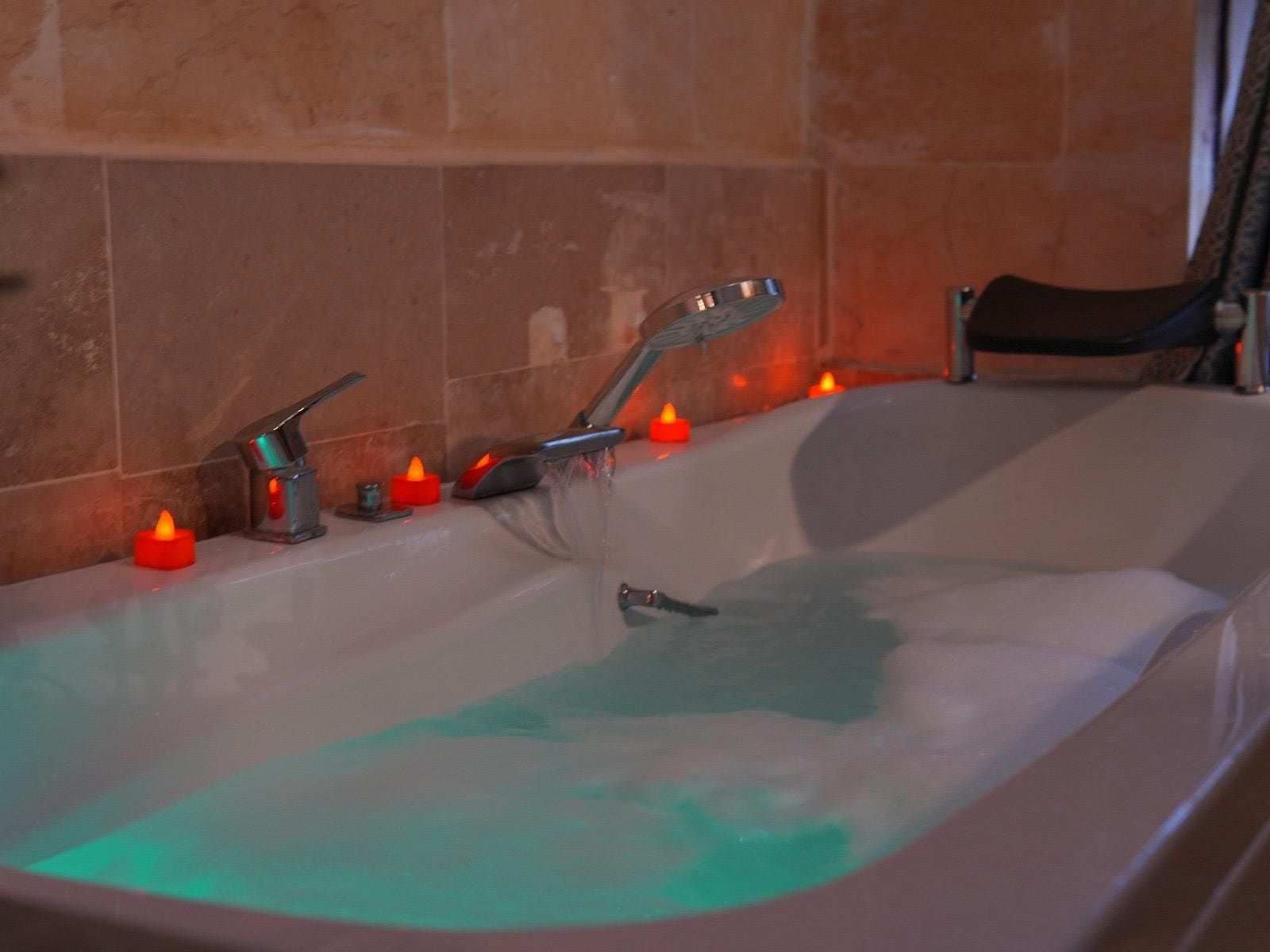 A bathtub with running water, a handheld showerhead, and multiple candles providing ambient lighting.