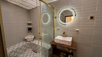 Un baño moderno con ducha de vidrio, un lavamanos blanco y una pileta estampada, y un espejo decorativo.