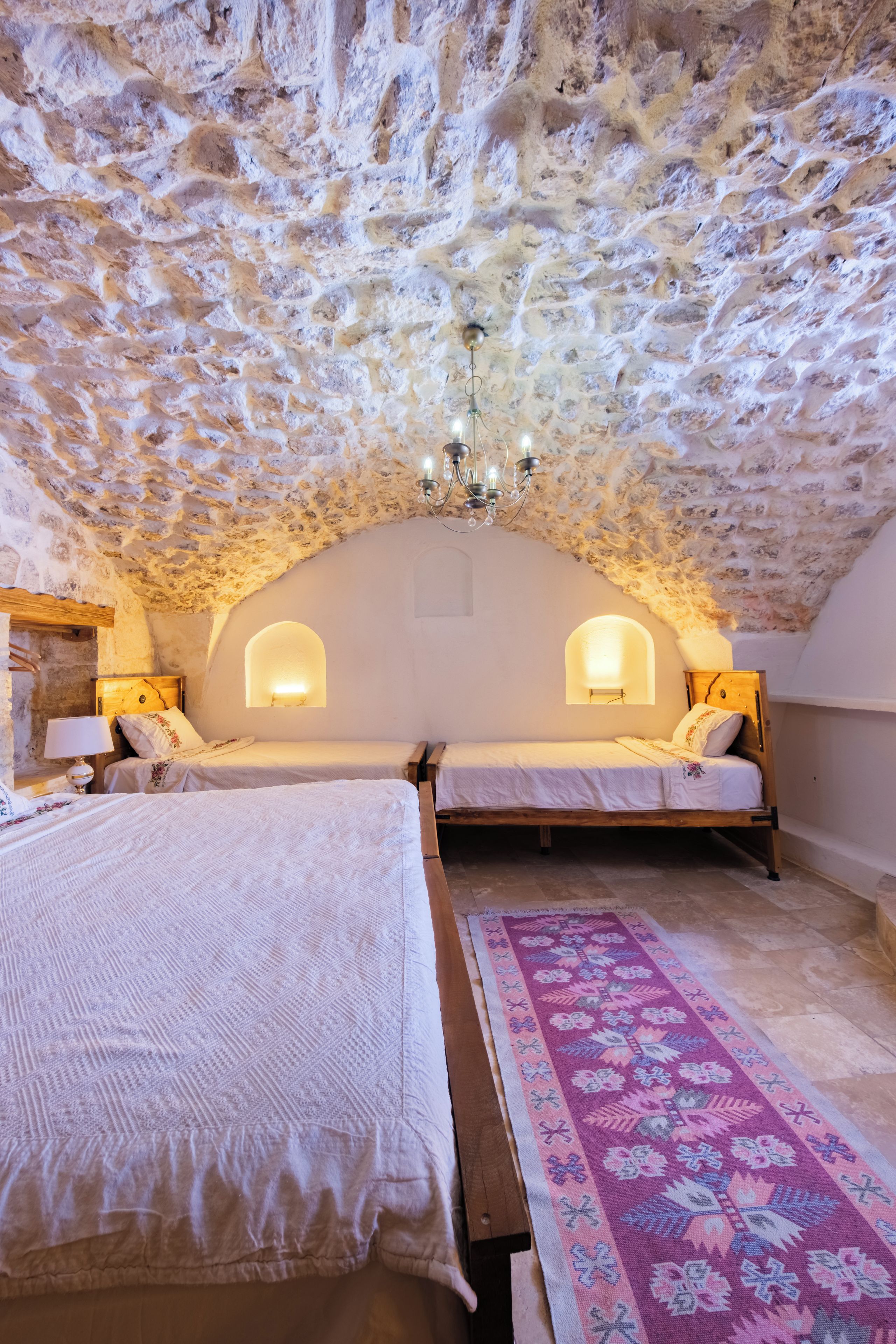 A bedroom with two beds, a patterned rug, and a stone ceiling.