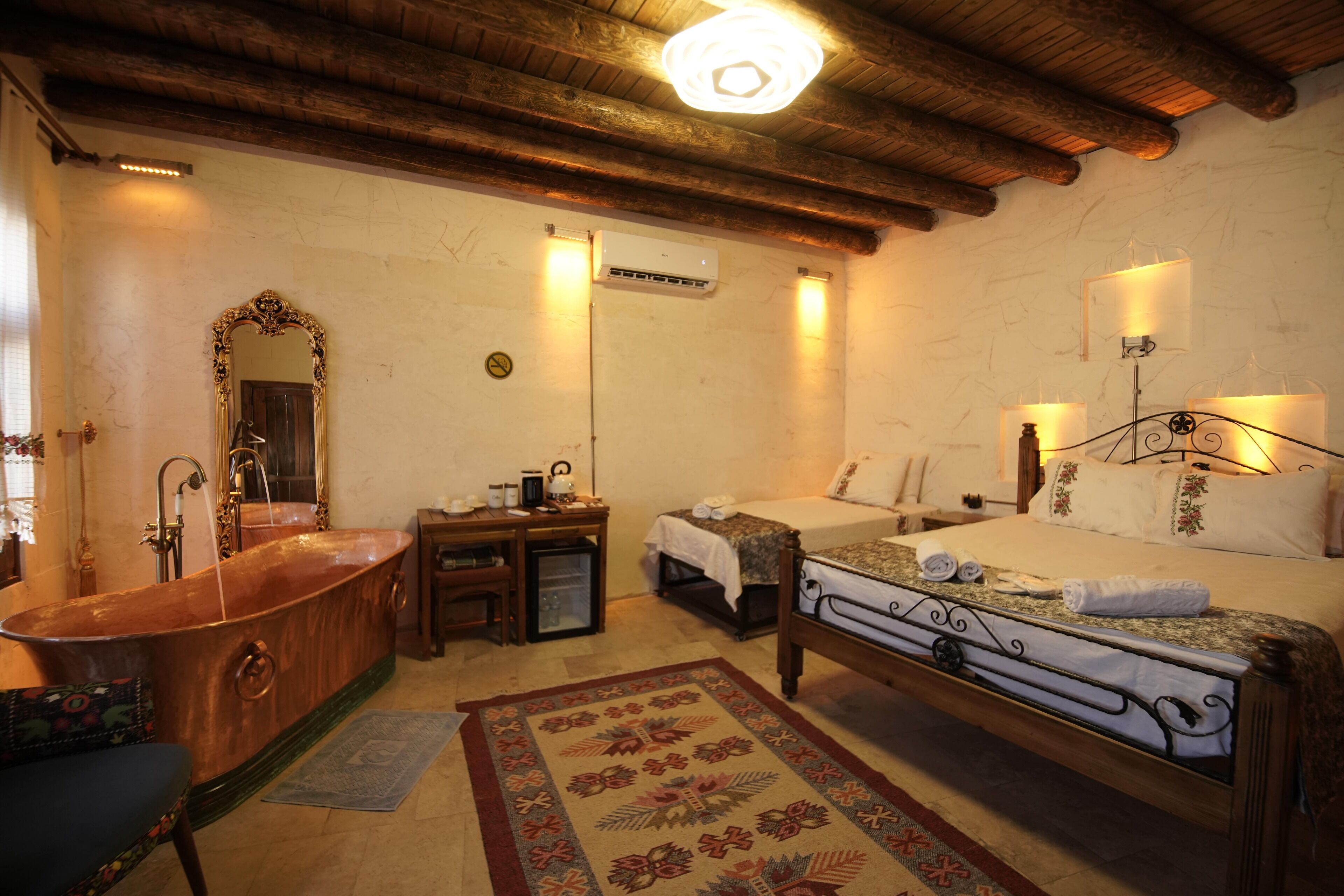 A traditional room with a large bathtub, a bed with a metal frame, a wooden desk, and a mirror.