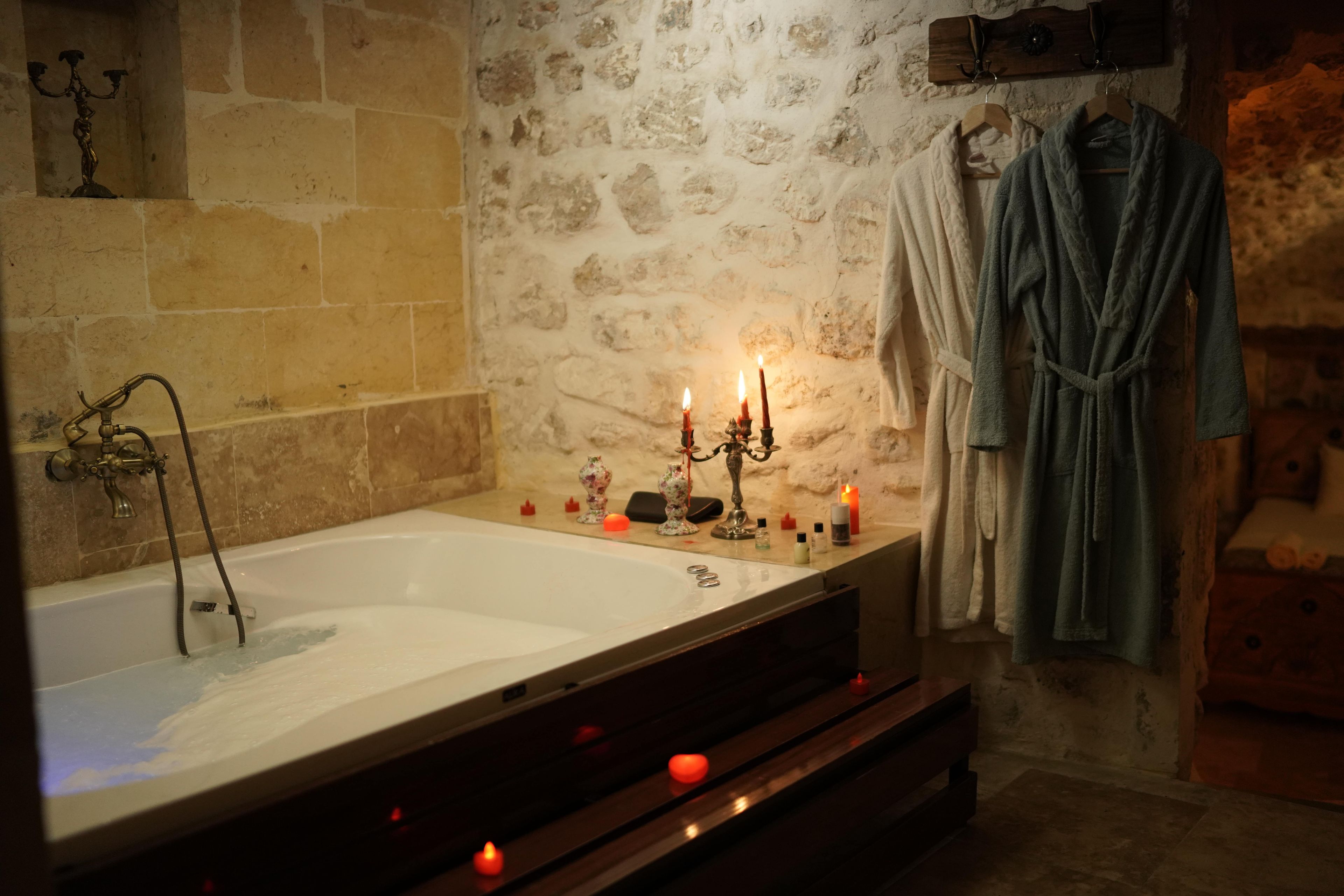 A bathroom with a bathtub, a shower, and a wooden bench. There are candles and toiletries on the bench.