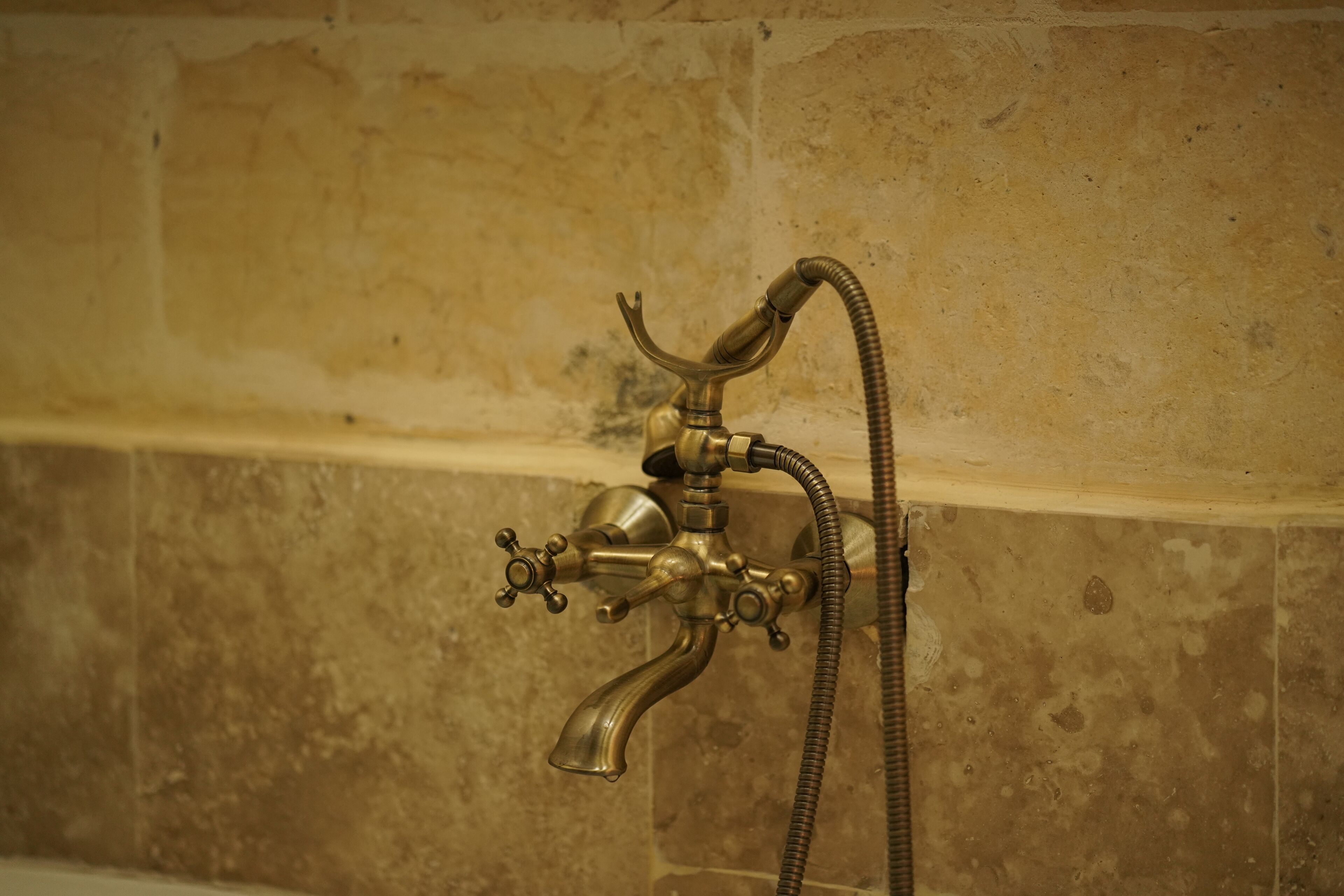 A brass bathroom fixture with a flexible hose, mounted on a tiled wall.