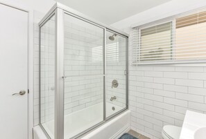 A bathroom with a glass-enclosed shower, white tiled walls, and a window with blinds. - West Newport Oceanfront Home & Patio on 65th St. (Newport Beach)