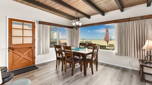 A dining area with a wooden table and chairs, a chandelier, and a view of the beach. - West Newport Oceanfront Home & Patio on 65th St. (Newport Beach)