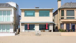A two-story house with a stone facade, large windows, and a balcony with red umbrellas. - West Newport Oceanfront Home & Patio on 65th St. (Newport Beach)